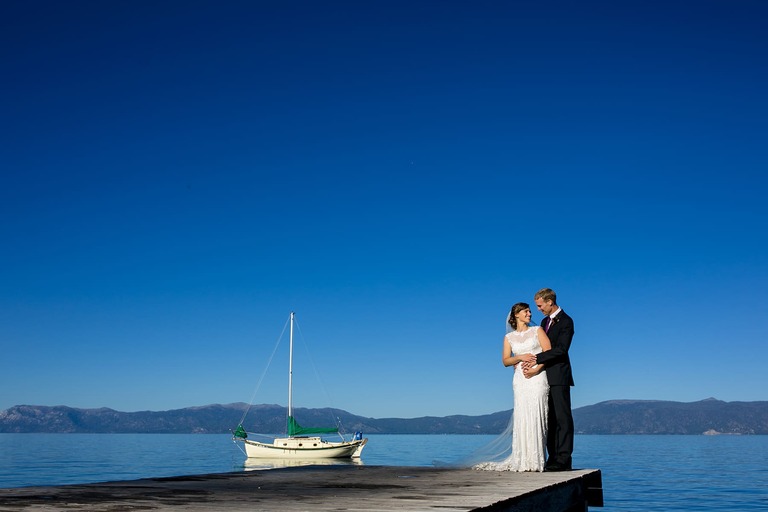 Standing on the Sugar Pine Point pier, a bride and groom share a romantic moment in front of a sailboat.