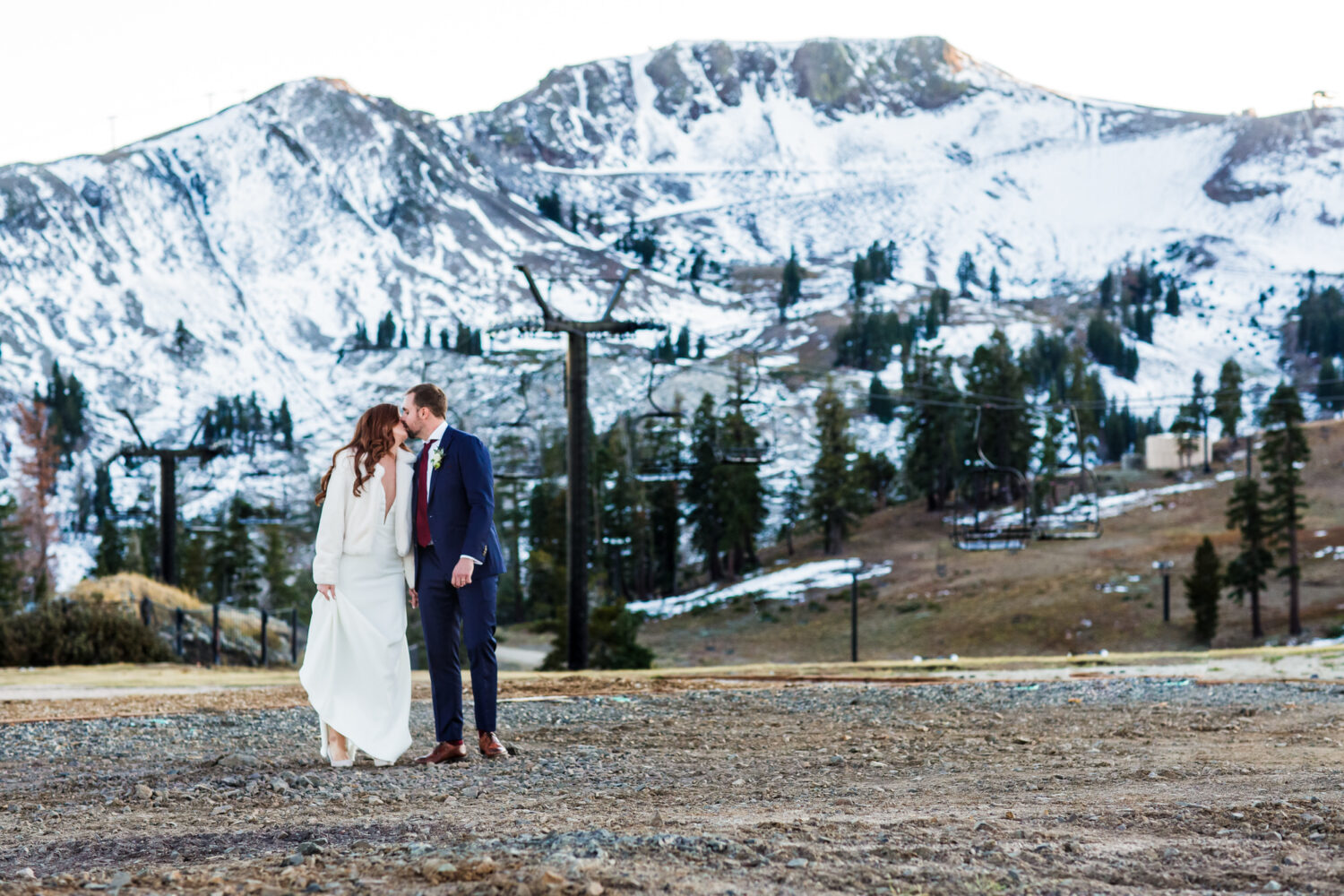 A romantic sunset walk for a bride and groom at Palisades Tahoe High Camp, with snowy mountains in the background.