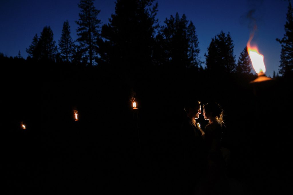 Nighttime portrait of a bride and groom with tiki torches.