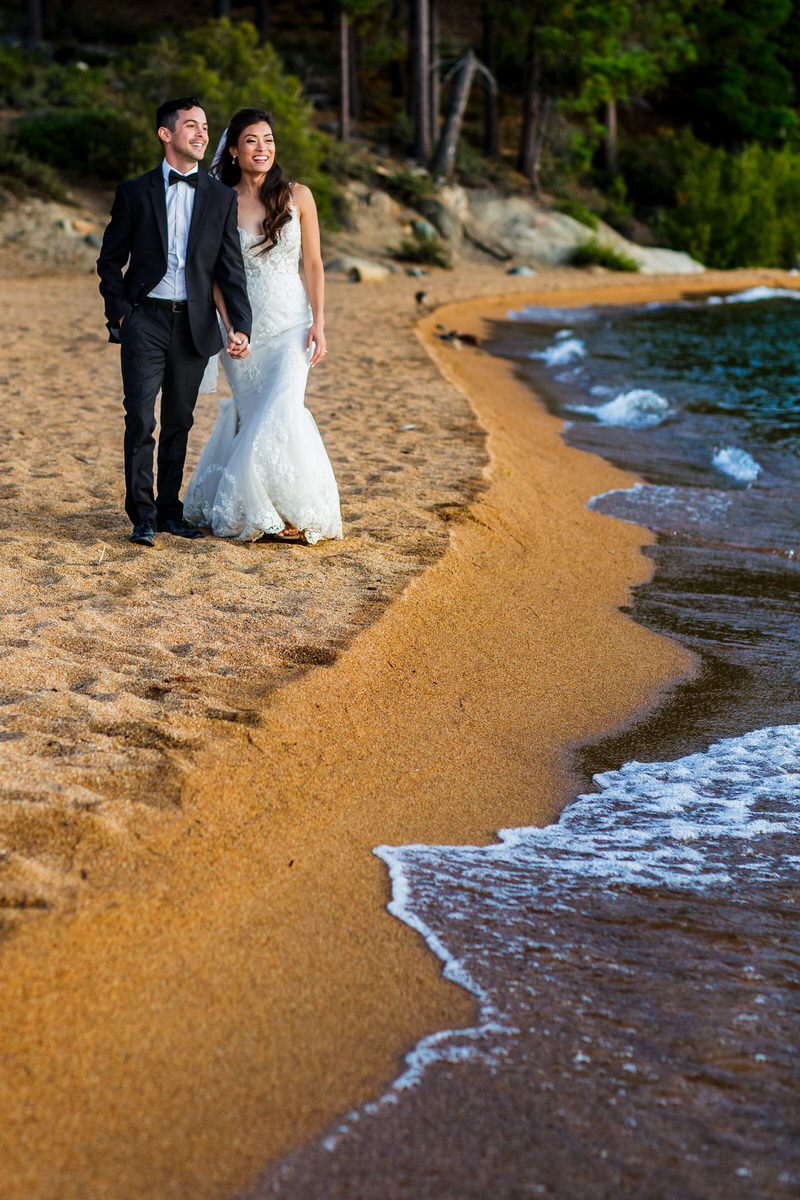 Bride and groom walk hand-in-hand at their lakeside beach wedding.