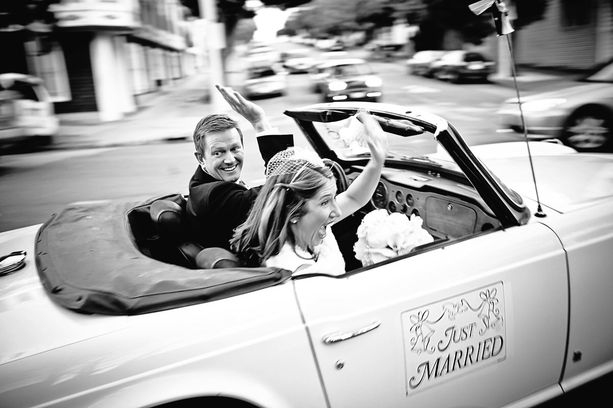 Bride and groom drive away in a convertible with a just married sign on the door.