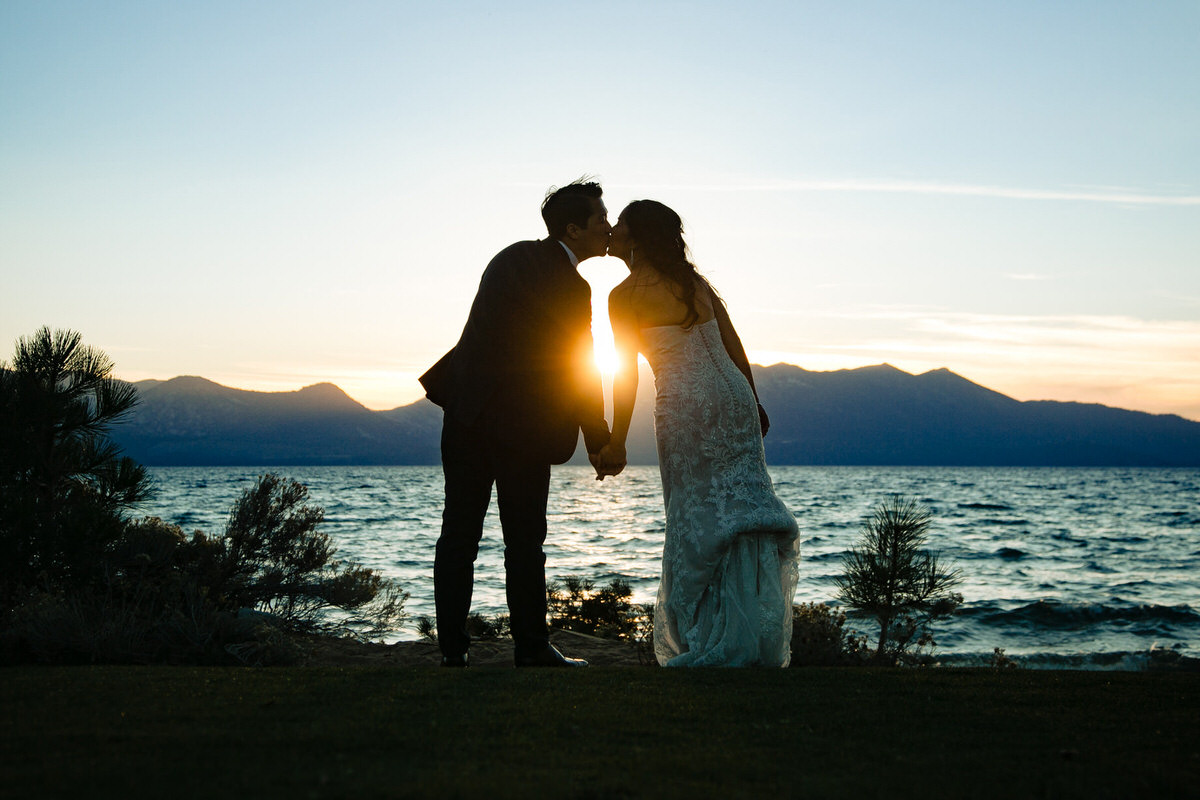 A romantic sunset kiss for a bride and groom at a lakefront wedding.