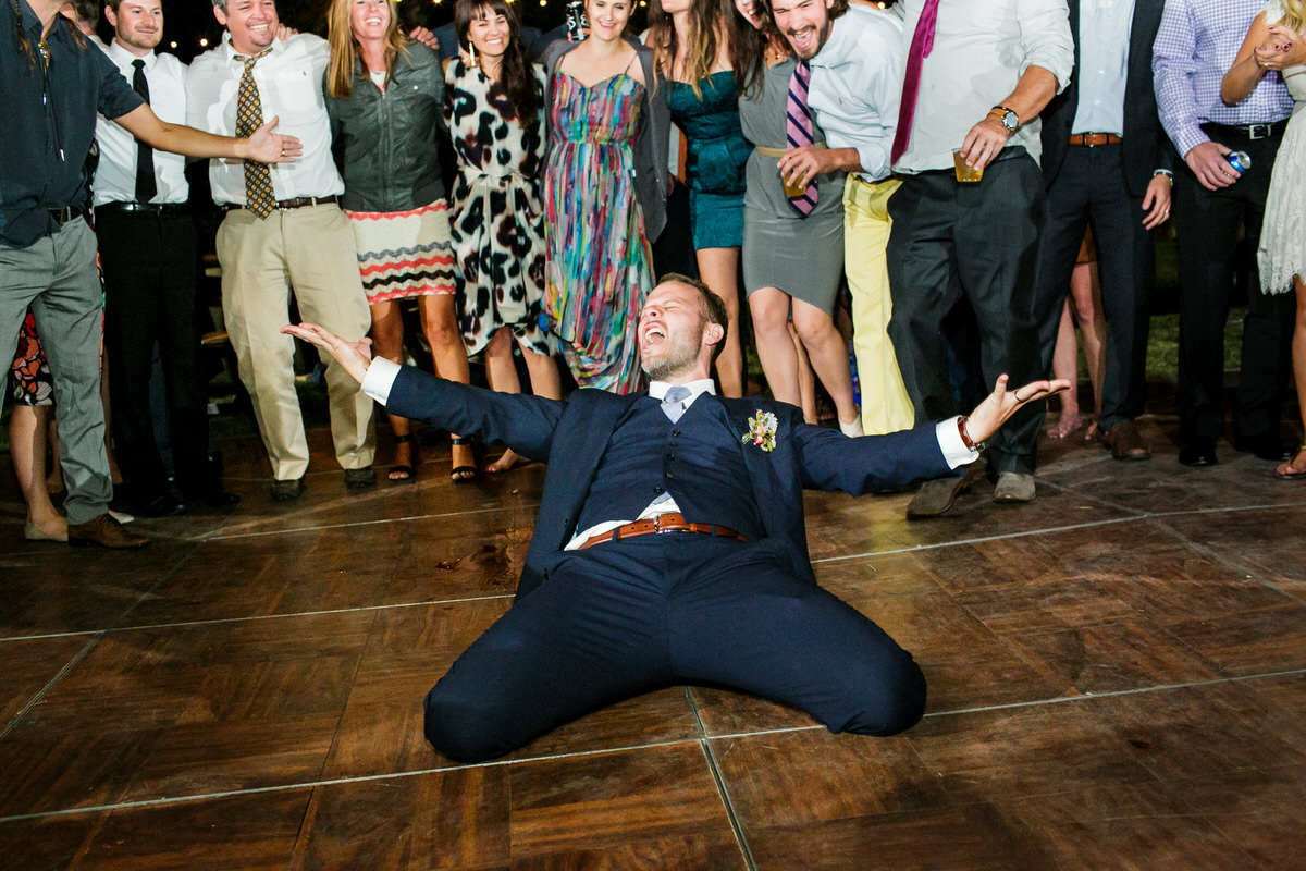 An ecstatic groom celebrates on a wooden dance floor.