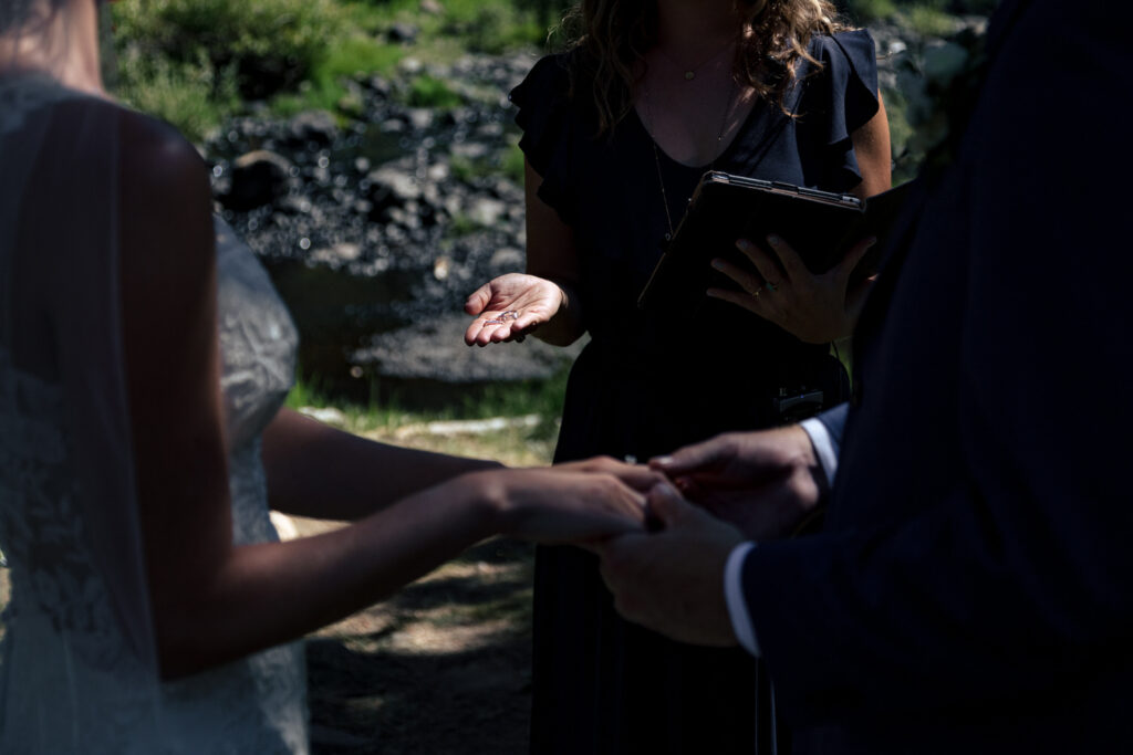 An officiant holds the bride and groom's wedding rings in a small beam of golden sunlight as they exchange vows.