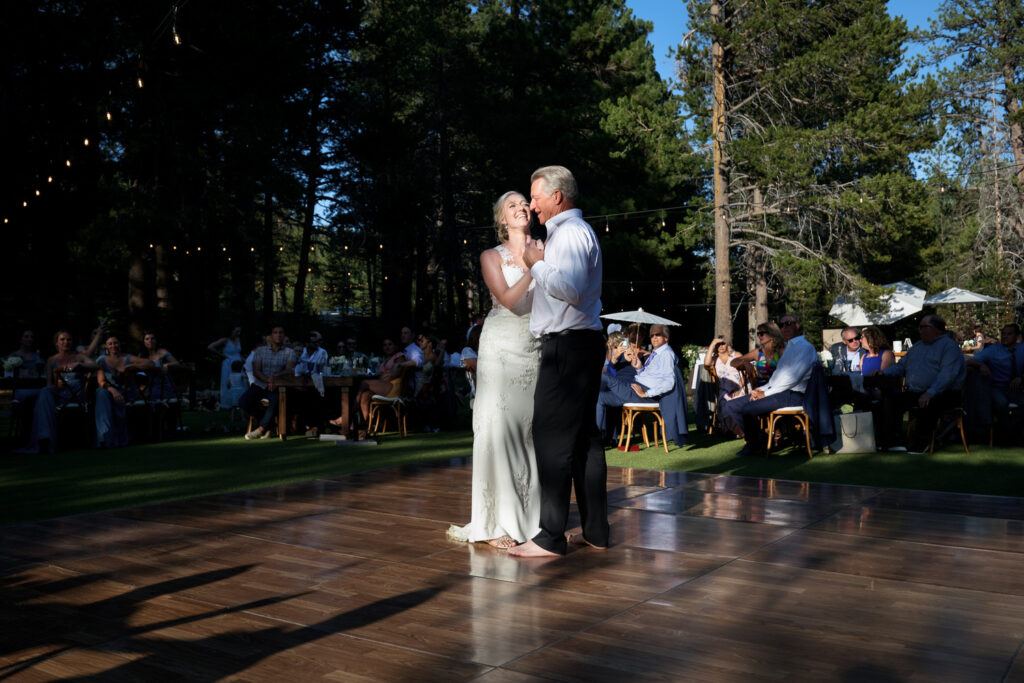 On the dance floor of an outdoor Dancing Pines wedding reception, the father of the bride dances with his daughter under the pine trees.