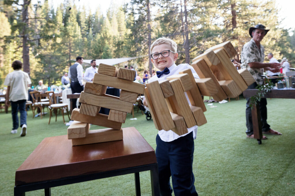 A young ring bearer plays an oversized game of Jenga at a Dancing Pines wedding reception.