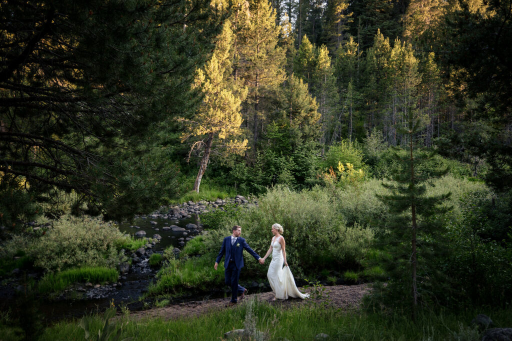The bride and groom walk hand-in-hand next to the Truckee River at Dancing Pines Resort, a wedding venue near Lake Tahoe, CA.