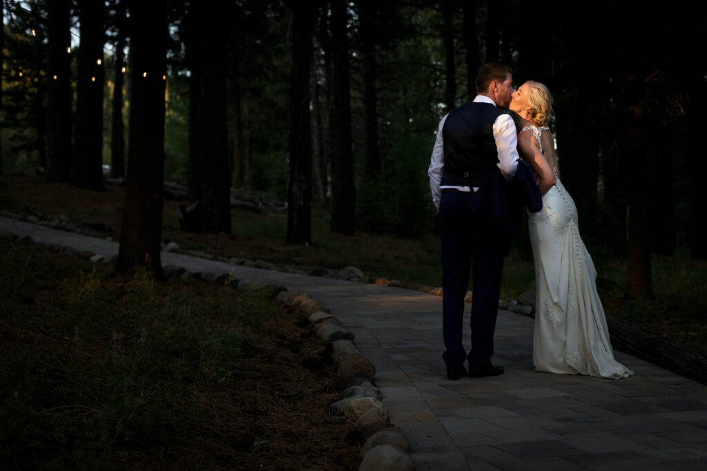 A bride and groom lean together for a kiss in a golden beam of sunlight among the trees at Dancing Pines Resort near Truckee, CA.