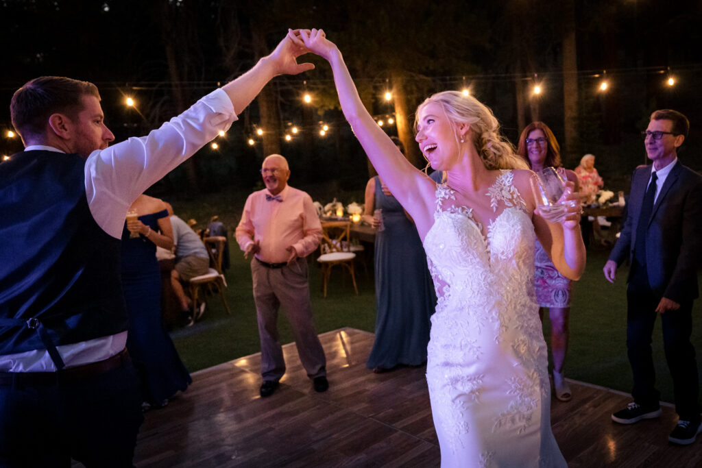 A groom and bride spin each other around on the center of the dance floor under colorful lights at Dancing Pines Resort.