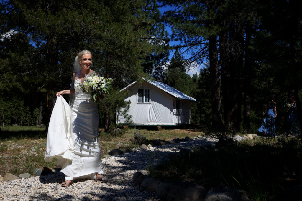 Passing through a ray of sunshine, a bride walks to the wedding ceremony site at Dancing Pines in Truckee, CA.