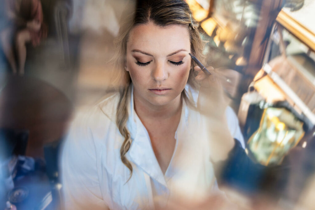 A photographer's creative view of a makeup artist applying eyeliner to a bride's eyes.