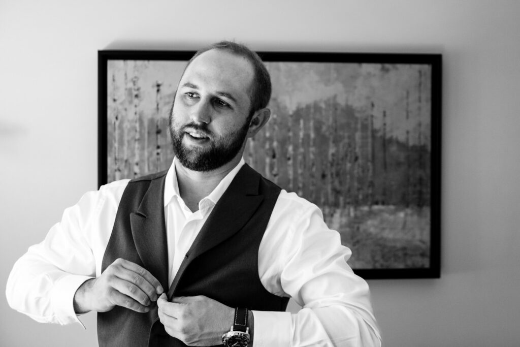 Black and white, candid portrait of the groom buttoning up his vest at a hotel room in Incline Village.