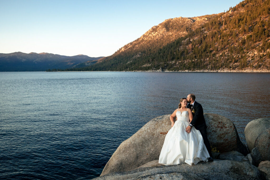 On the shore of Lake Tahoe, a bride and groom  share a romantic moment at sunset.