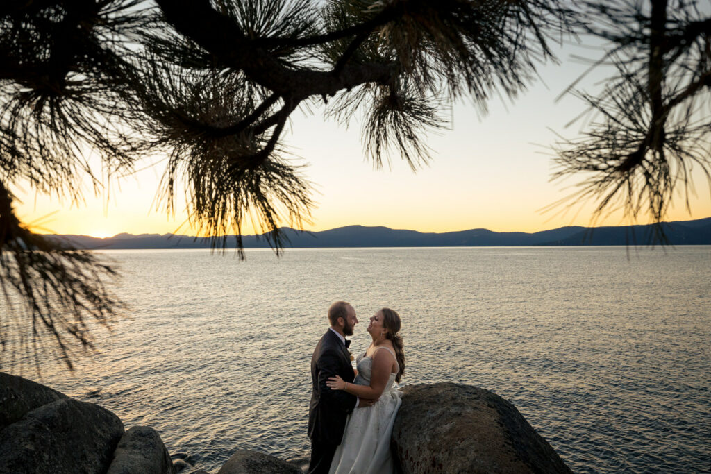 Pine trees frame a bride and groom at sunset along the shore of Lake Tahoe after their Thunderbird Lodge wedding.