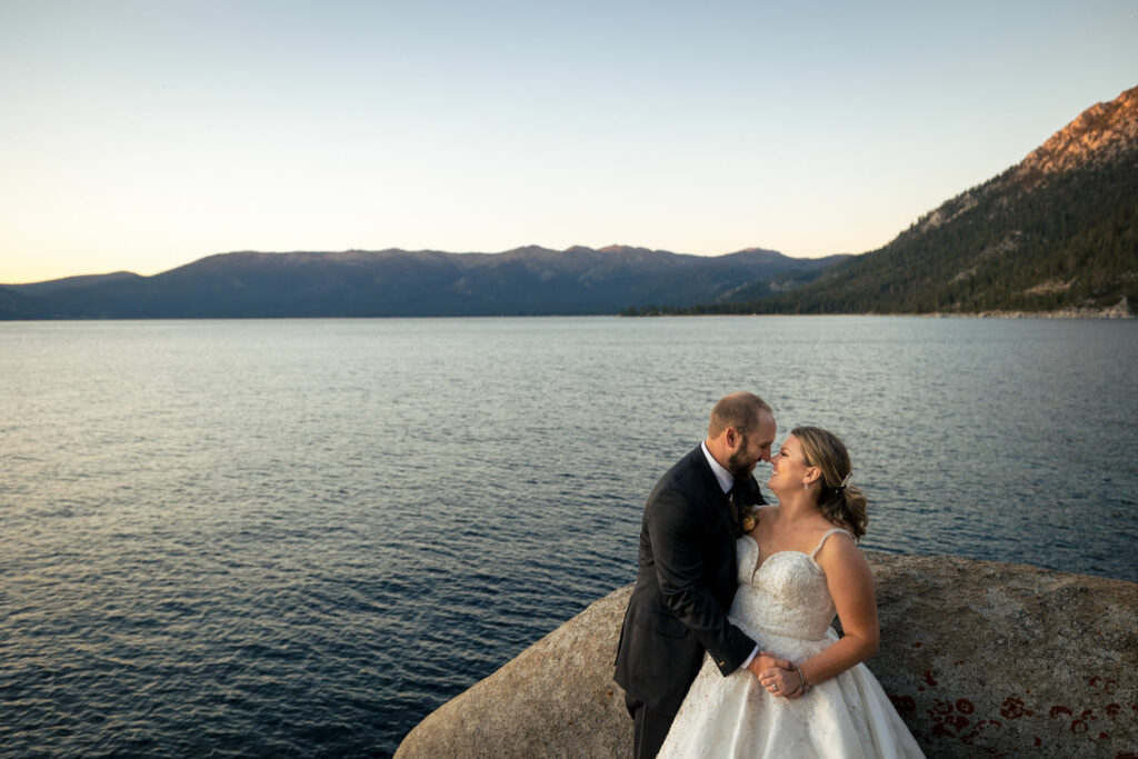 A bride and groom laugh together in front of Lake Tahoe at sunset.