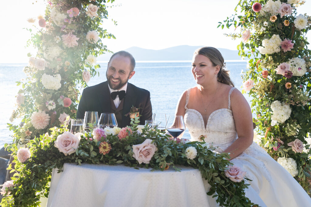 A bride and groom smile at the sweetheart table at their outdoor Thunderbird Lodge wedding reception.