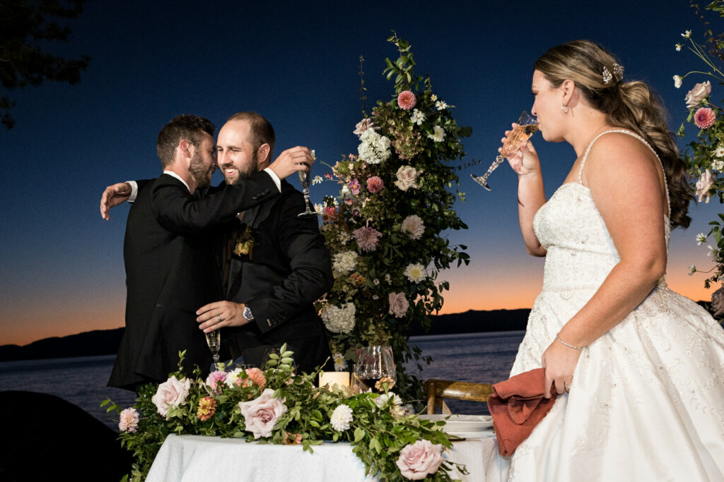 The bride sips champagne while the groom hugs his best man after delivering a speech at the wedding reception.