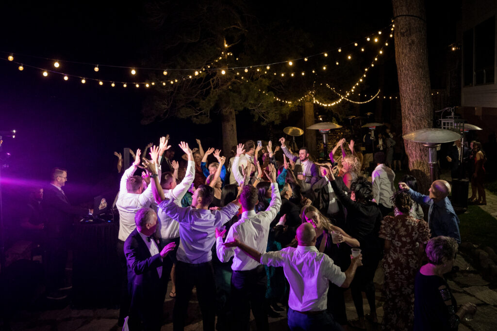 Colorful lights from a Lake Tahoe DJ illuminate the dance floor at an outdoor Thunderbird Lodge wedding.