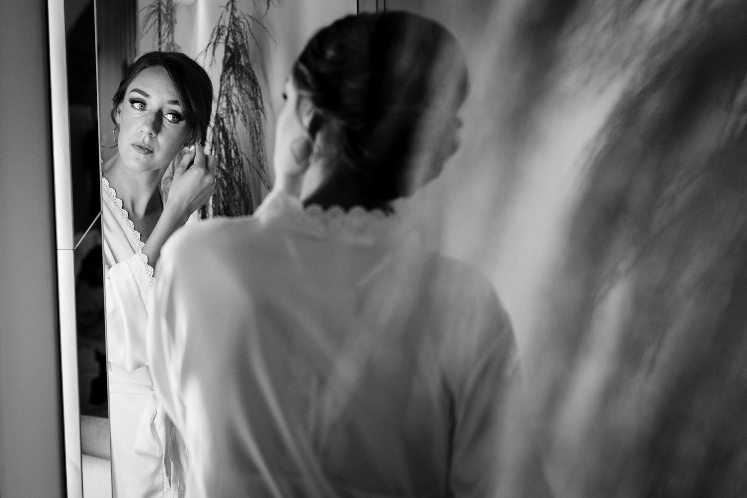 Black and white portrait of a bride looking in a mirror and putting on earrings at Chalet View Lodge near Blairsden-Graeagle.