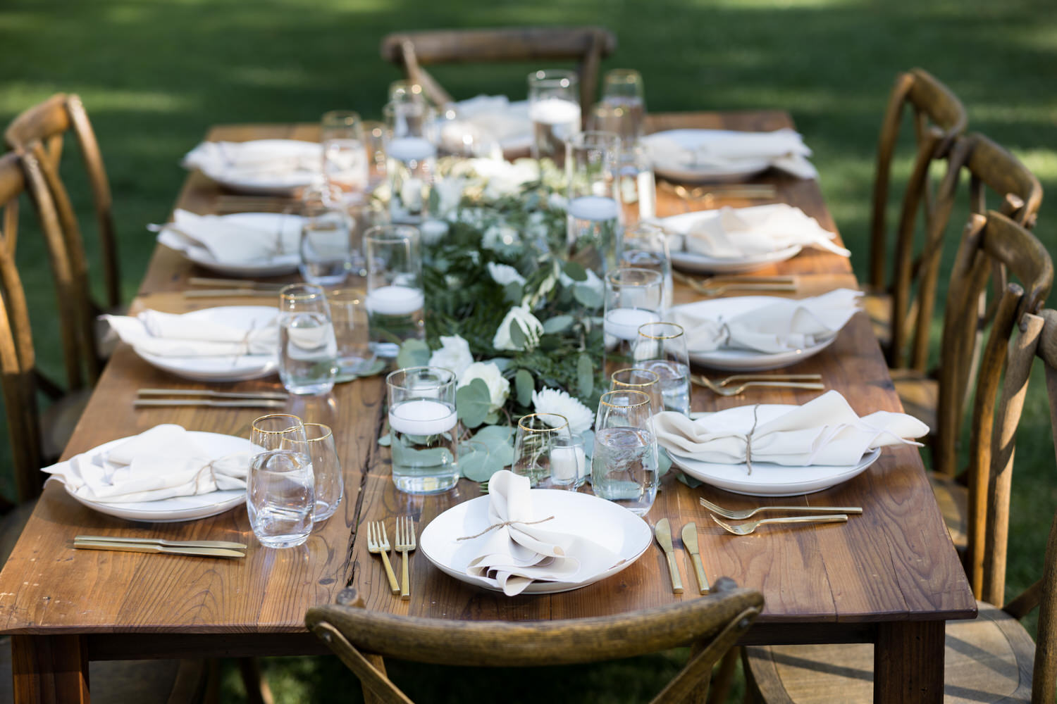 An example of a wedding reception table setting at Chalet View Lodge with wooden banquet tables and chairs, with golden flatware and gold-rimmed glasses. 