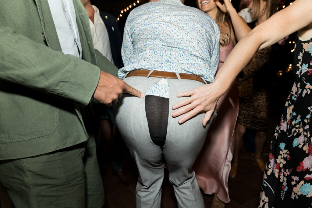 As the dancing heats up, wedding guests on the dance floor point at the torn seat of a man's pants.