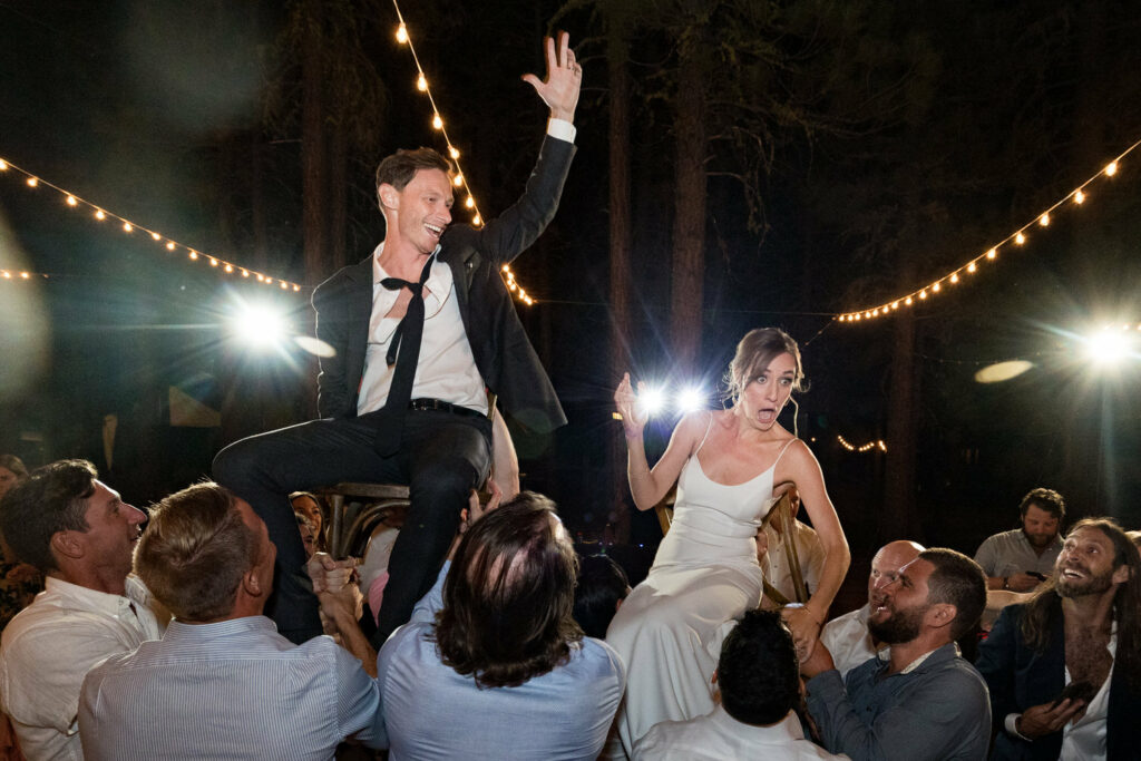 The groom and bride make funny, surprised faces as their friends lift them up on chairs during their Chalet View Lodge wedding reception.