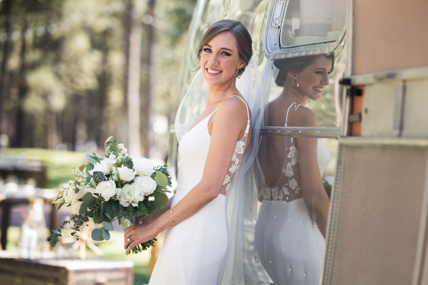 A bride poses for a portrait next to a silver airstream trailer.