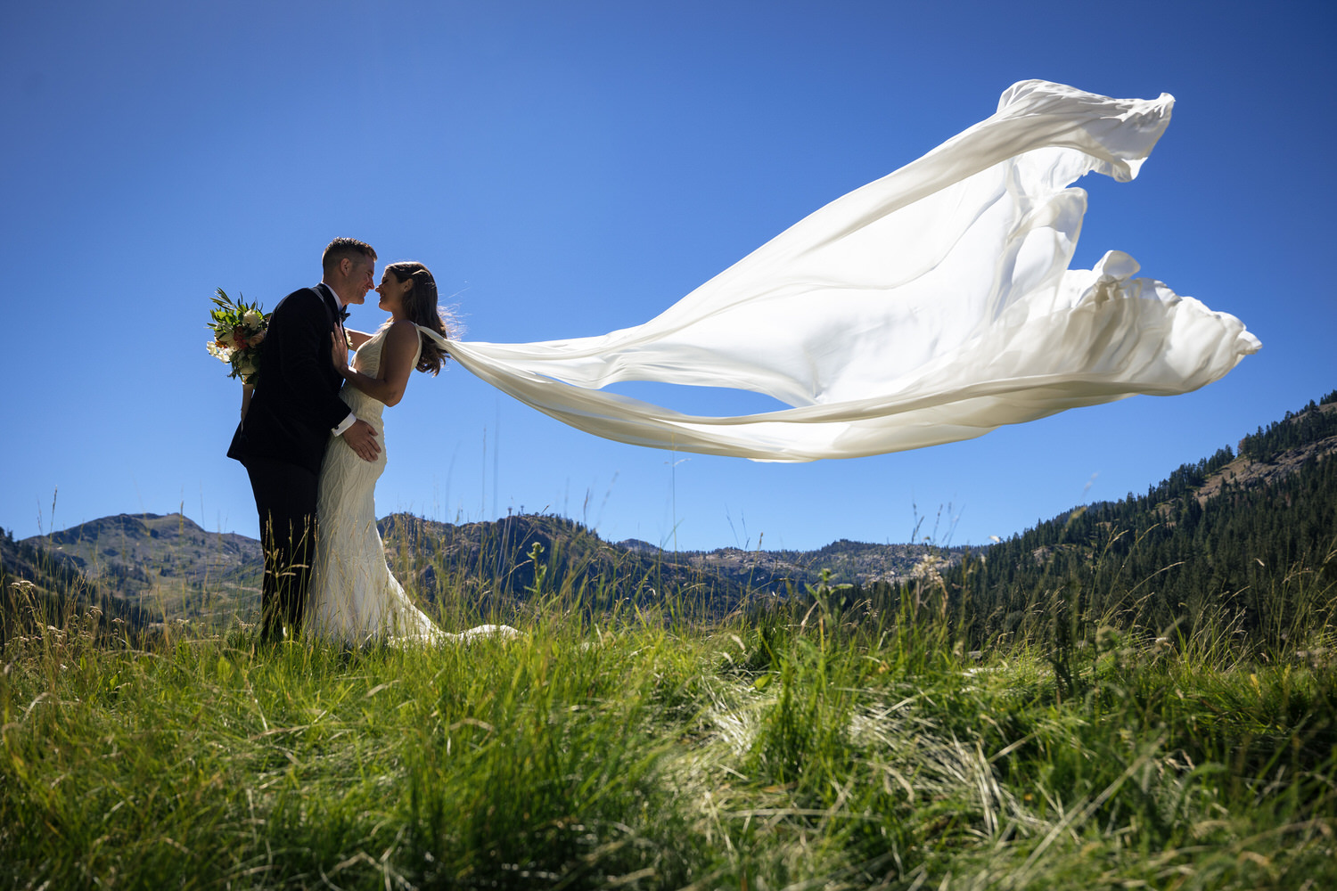 As the couple embraces, a bride's white chiffon bridal wings fly up into the air behind her.