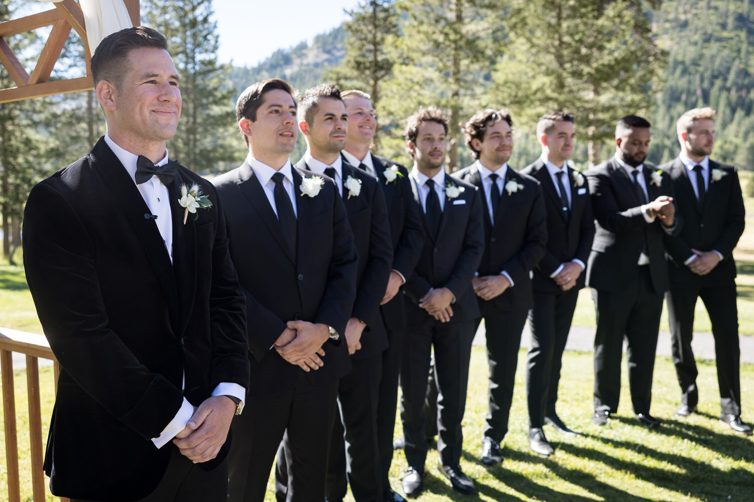 A groom and his eight groomsmen wait for the bride to arrive at an outdoor black tie wedding ceremony.