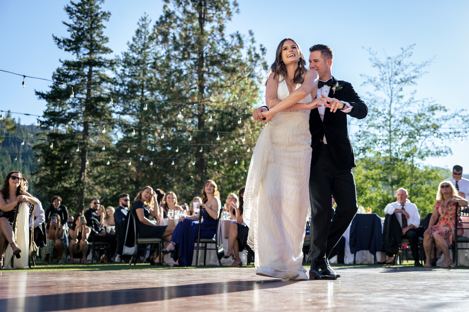 A happy bride and groom enjoy their first dance as husband and wife at an outdoor wedding reception under the pine trees.