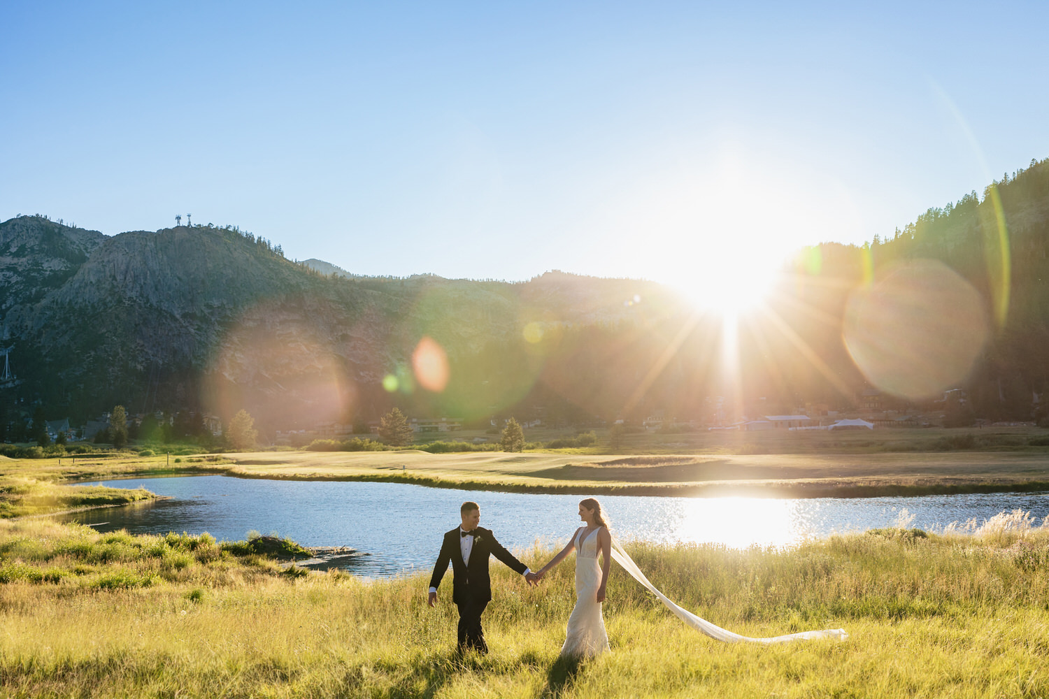 A groom leads his bride through a golden meadow in Olympic Valley as the sun sets behind Granite Chief peak.