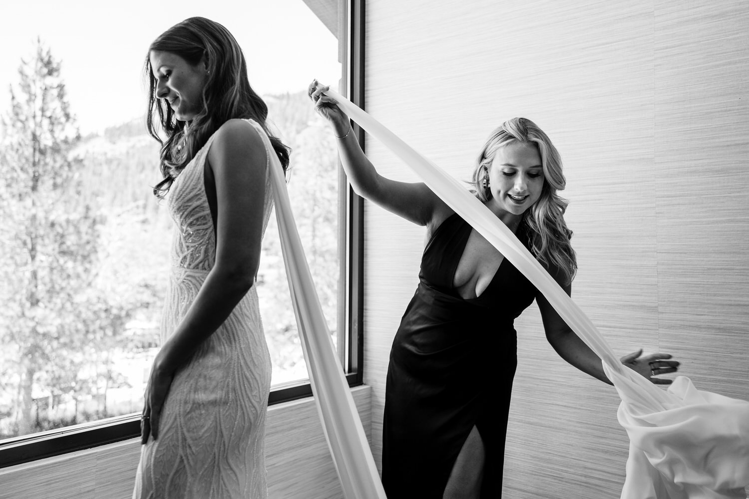 A maid of honor helps pin long, white chiffon bridal wings to the back of the bride's dress.