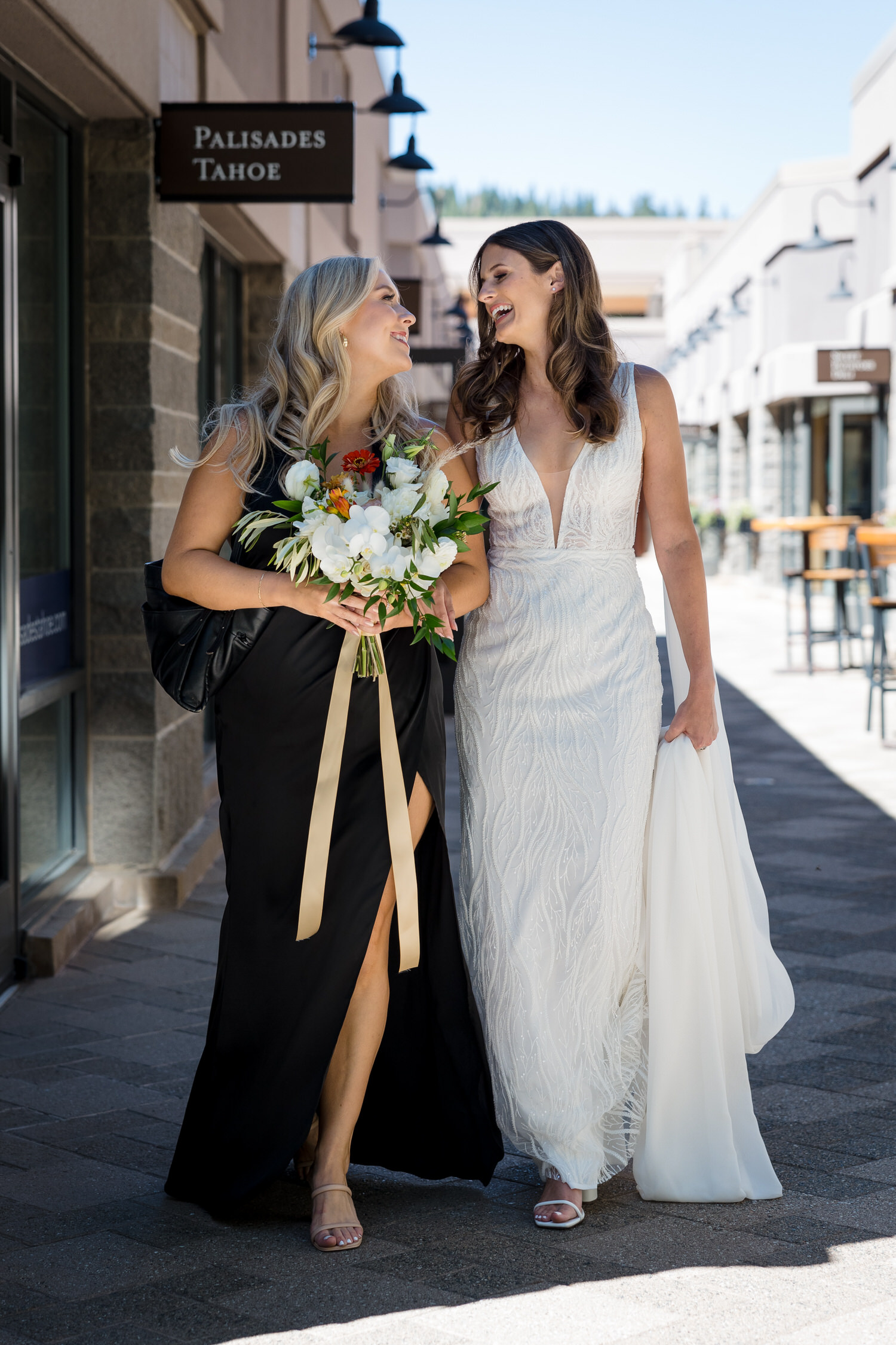 A bride and her maid of honor share a loving moment of friendship as they walk past shopping at Everline Resort and Spa.
