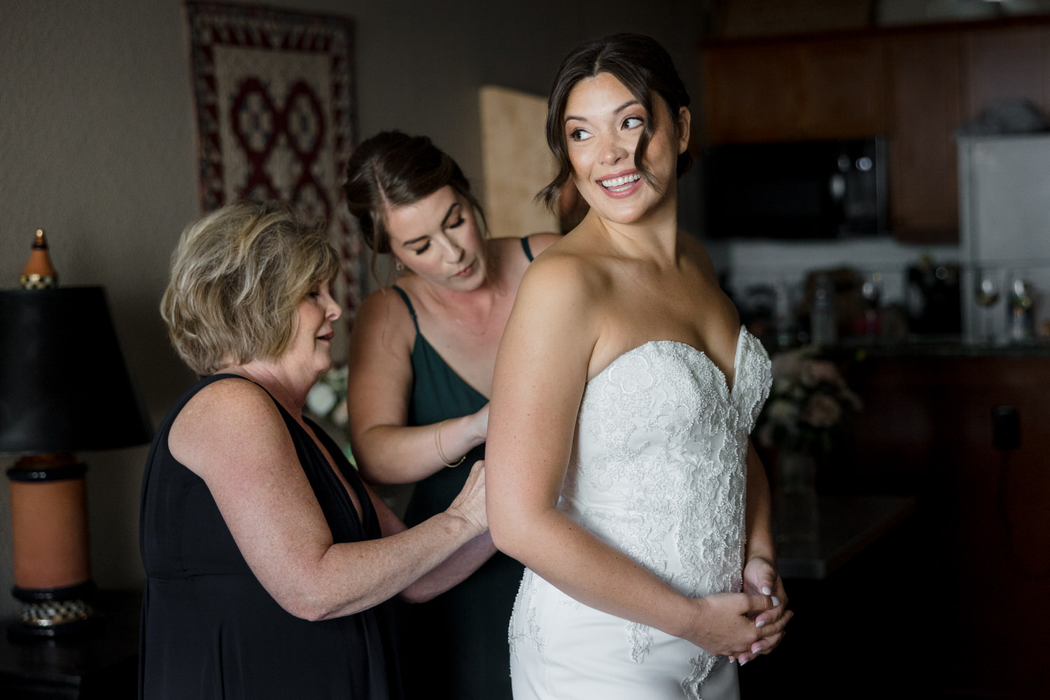 A mom and sister help the bride with her wedding dress in a hotel room in the Village at Palisades Tahoe.
