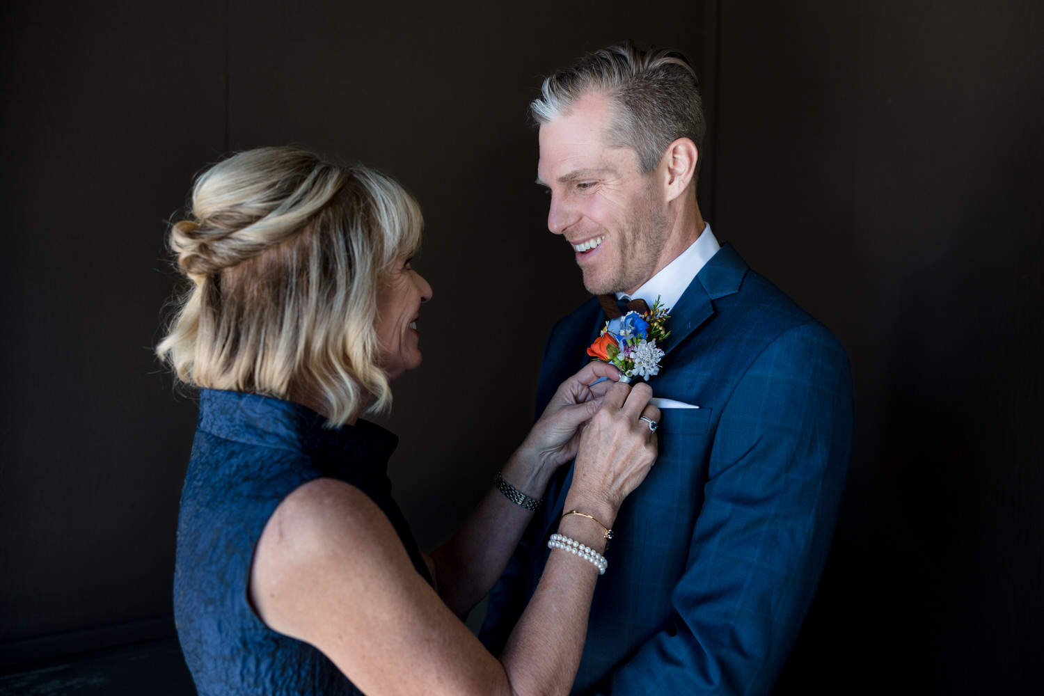 Mom pinning the groom's colorful flower boutonnière on his jacket lapel.