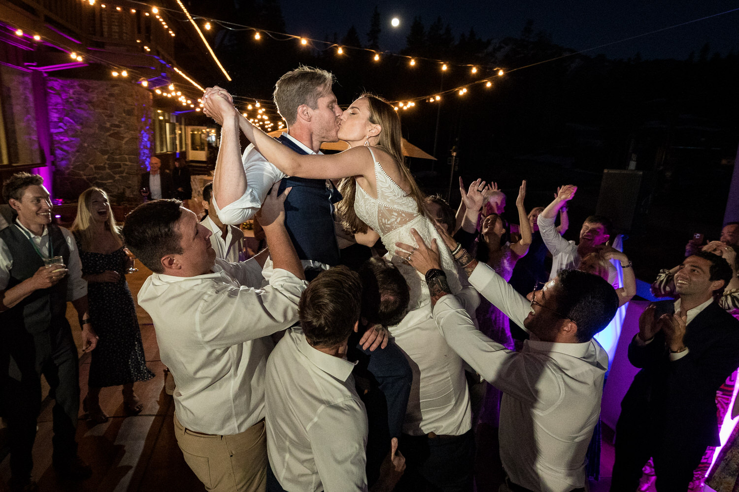 Wedding guests lift the bride and groom on their shoulders for a memorable wedding kiss.