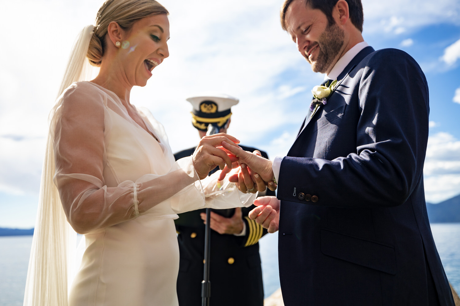 Low angle view of the bride placing a wedding ring on the groom's finger with Lake Tahoe in the background.