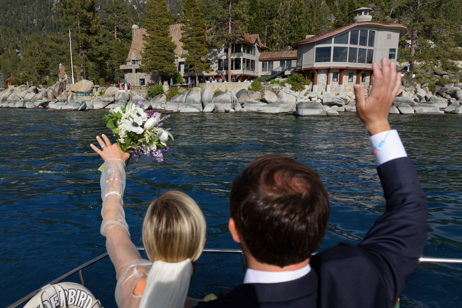 A bride and groom aboard the Thunderbird Yacht wave to wedding guests on the lawn.