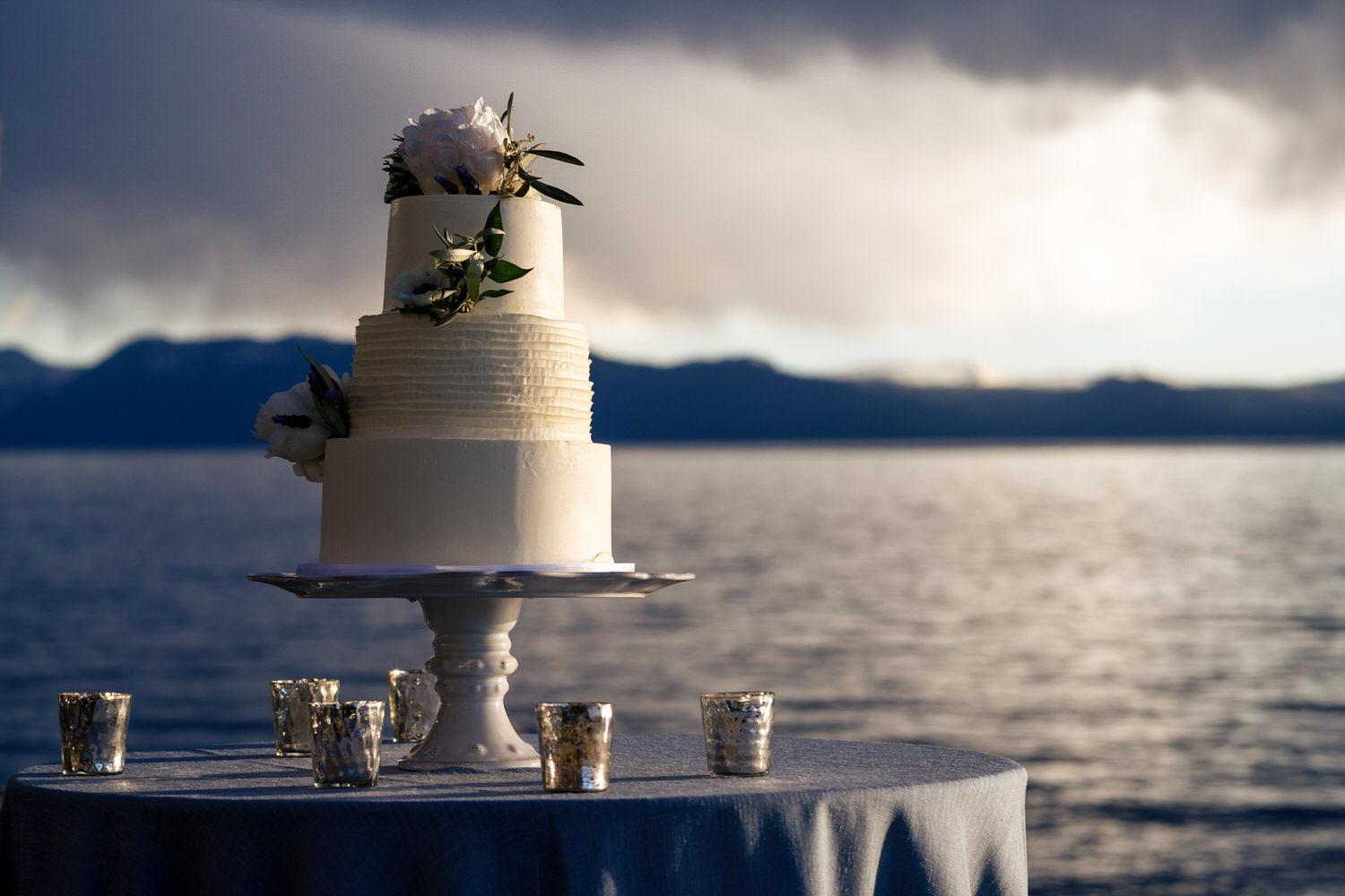Three tier wedding cake on a table with Lake Tahoe in the background.