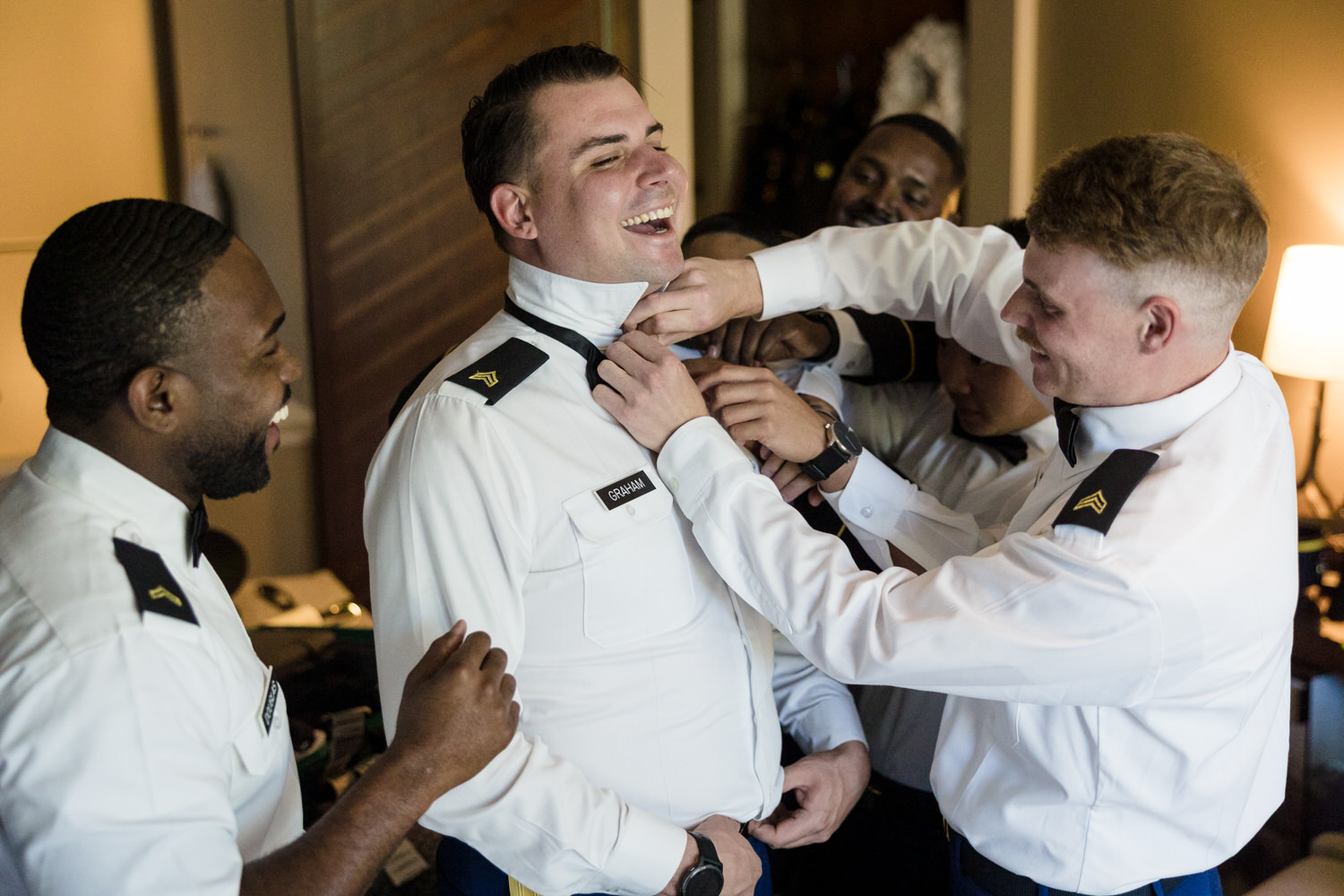 Groomsmen in air force dress blues help the groom get dressed.