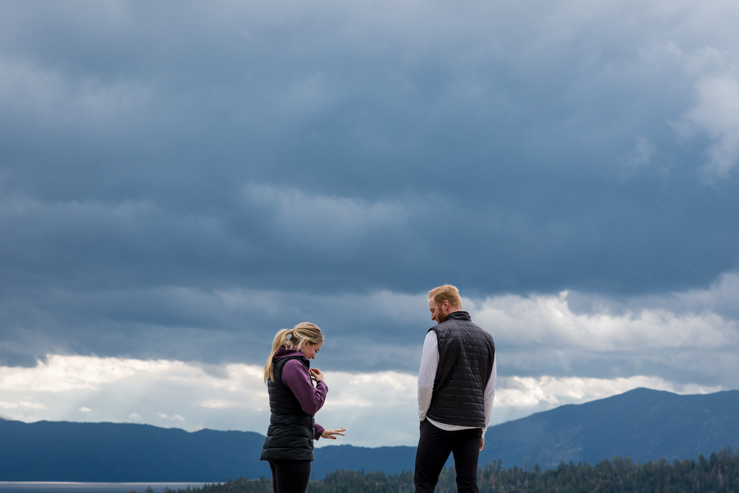 A candid moment admiring the engagement ring at a surprise proposal in front of Lake Tahoe on a cloudy day.