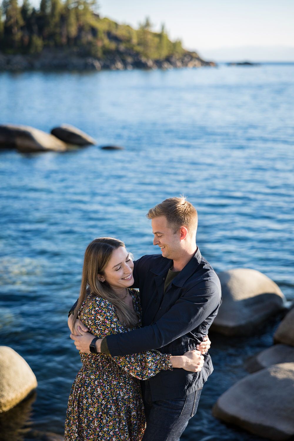 A couple enjoys a quiet, happy moment at their surprise proposal next to a lake.