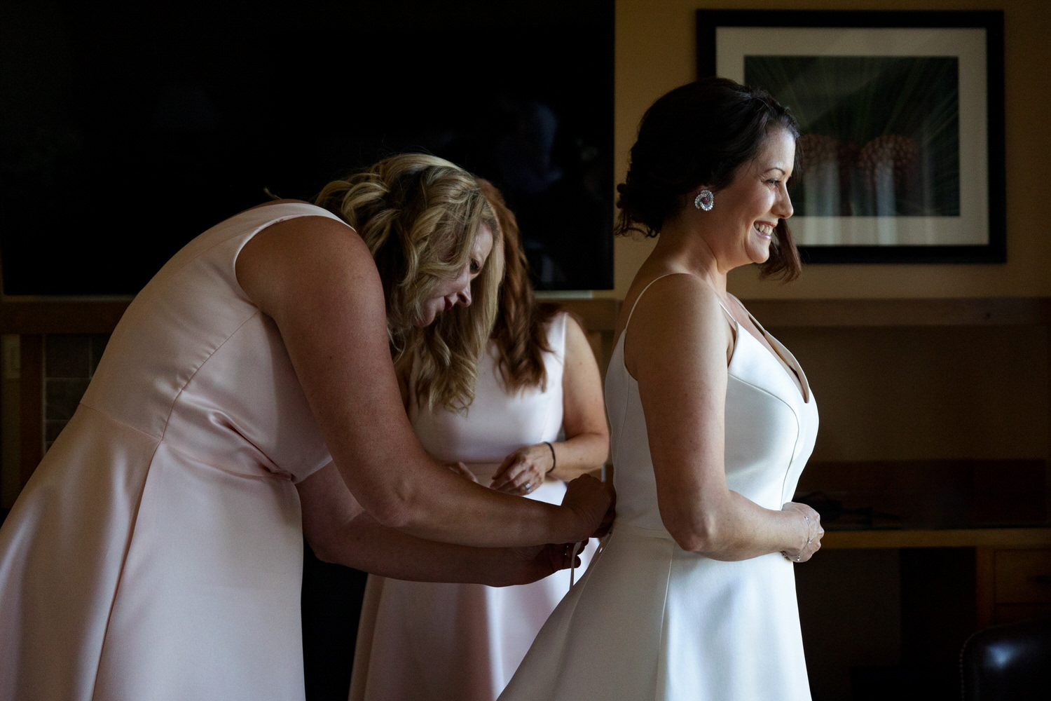 Bridesmaids help the bride lace up the back of her wedding dress in a Ritz Carlton hotel room.