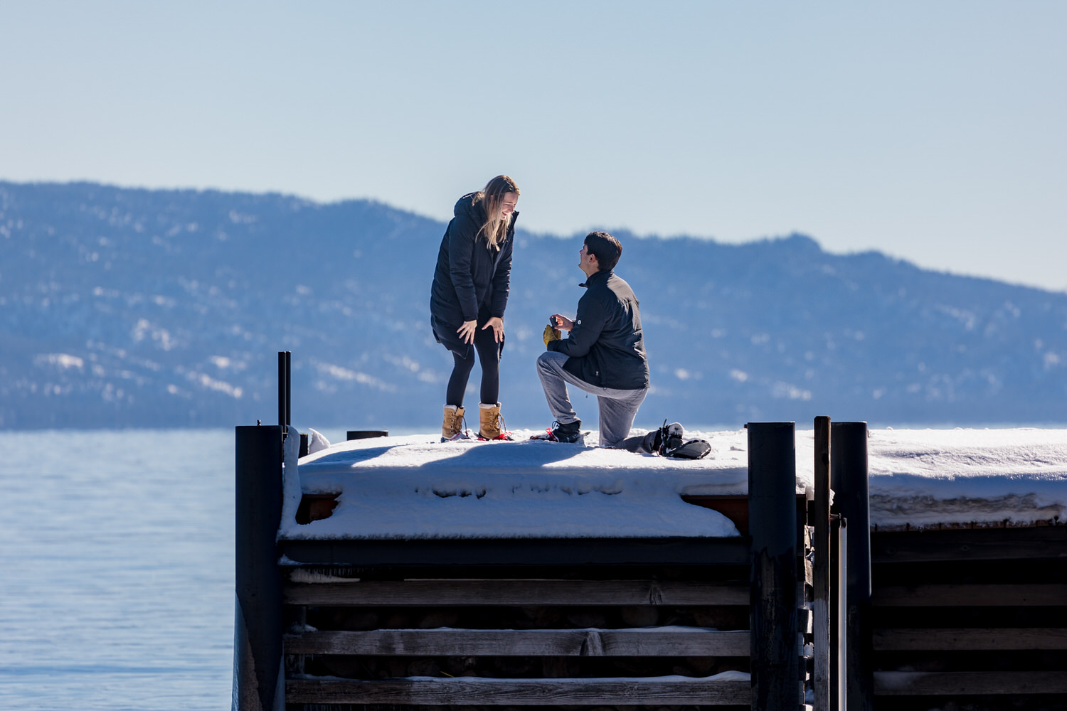 Surprise wedding proposal during winter on a lake pier.