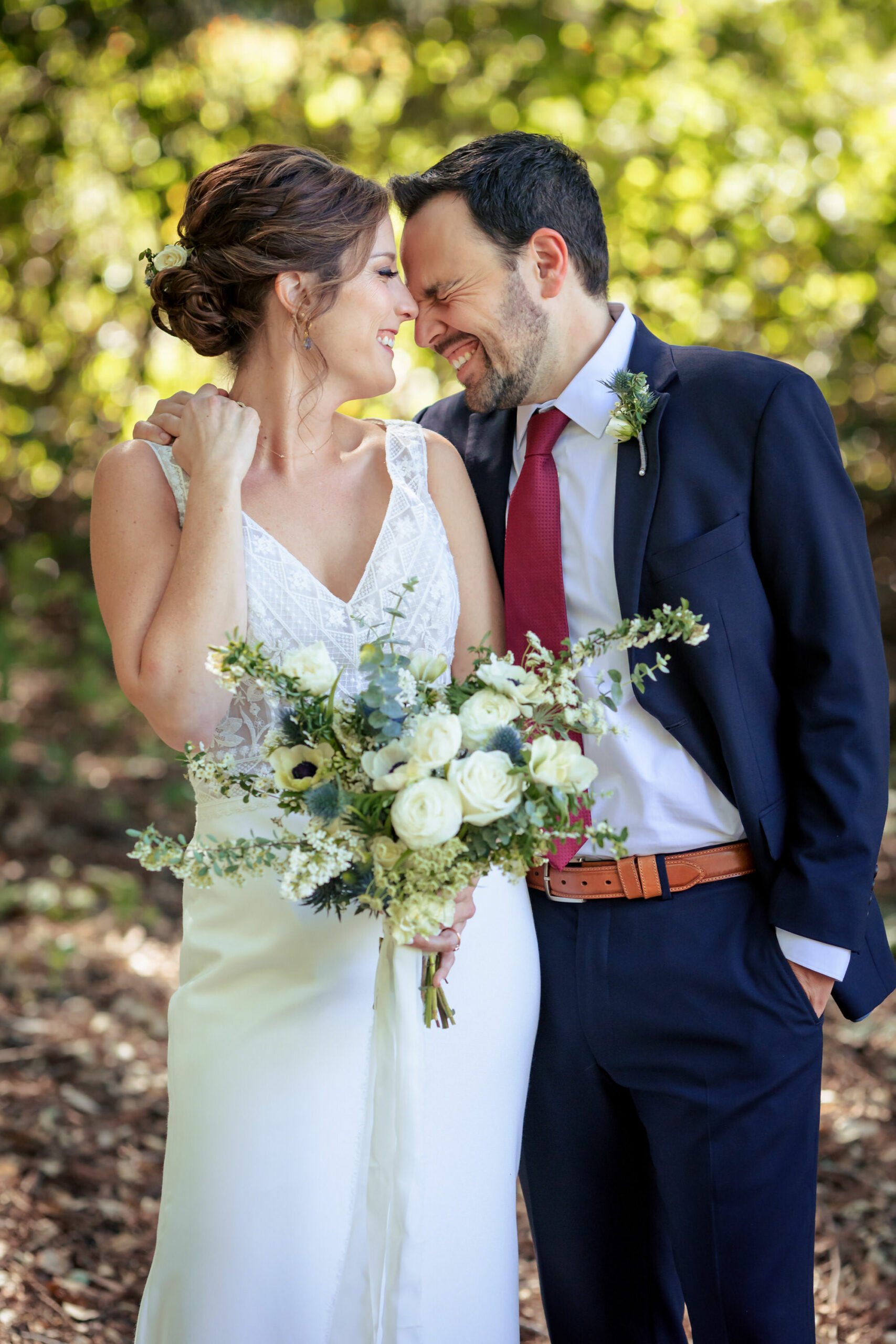 Candid moment of a bride in a lace top wedding dress and a groom wearing a navy blue suit with a red tie.