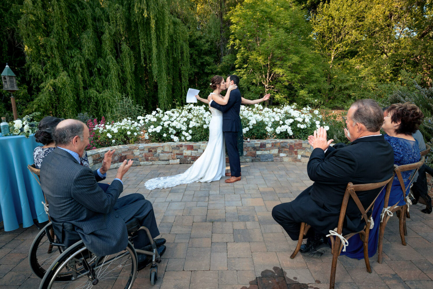 Wide angle view of a first kiss at an intimate wedding on a garden patio. 