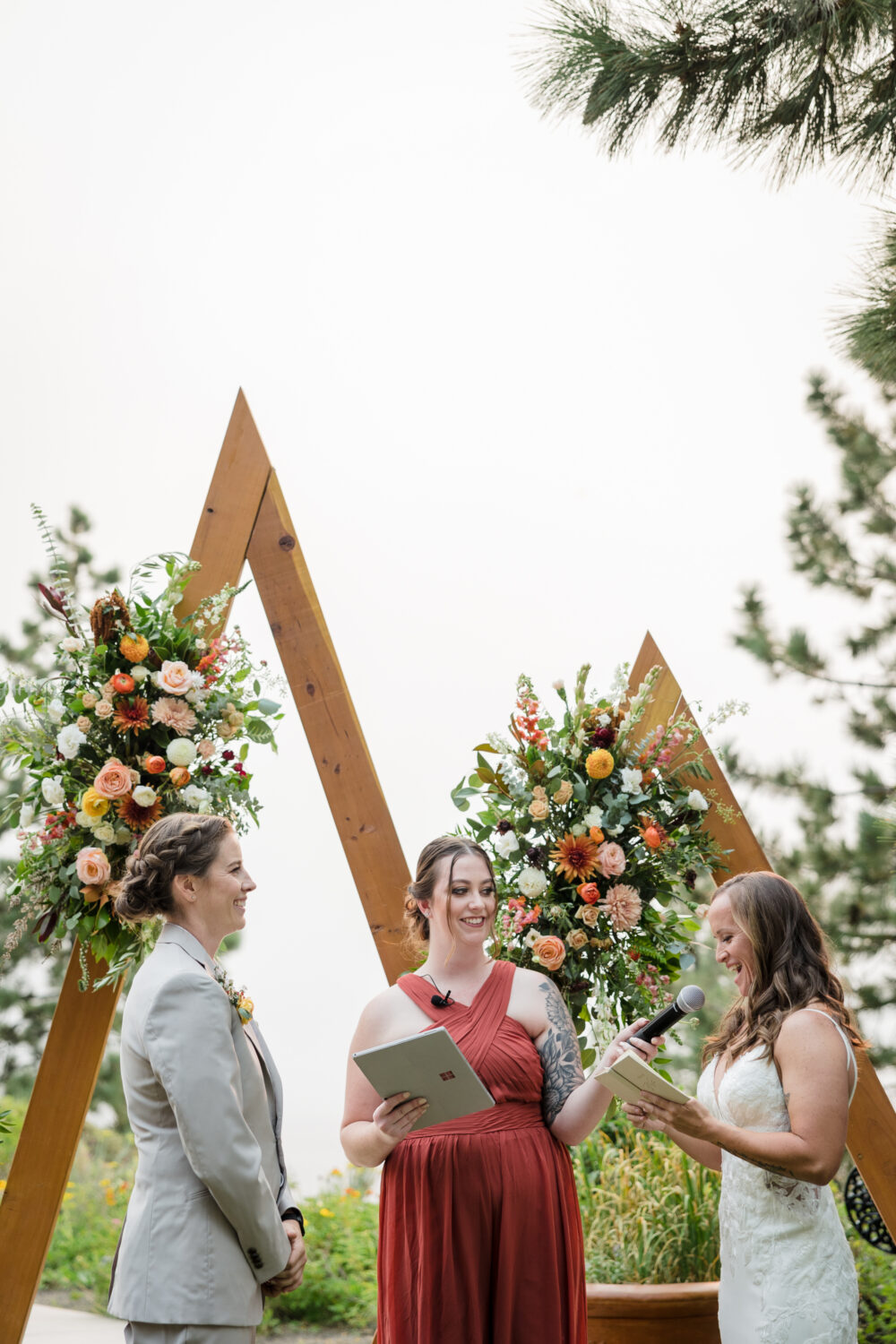 Two brides exchange vows in front of two triangular wooden wedding arches.