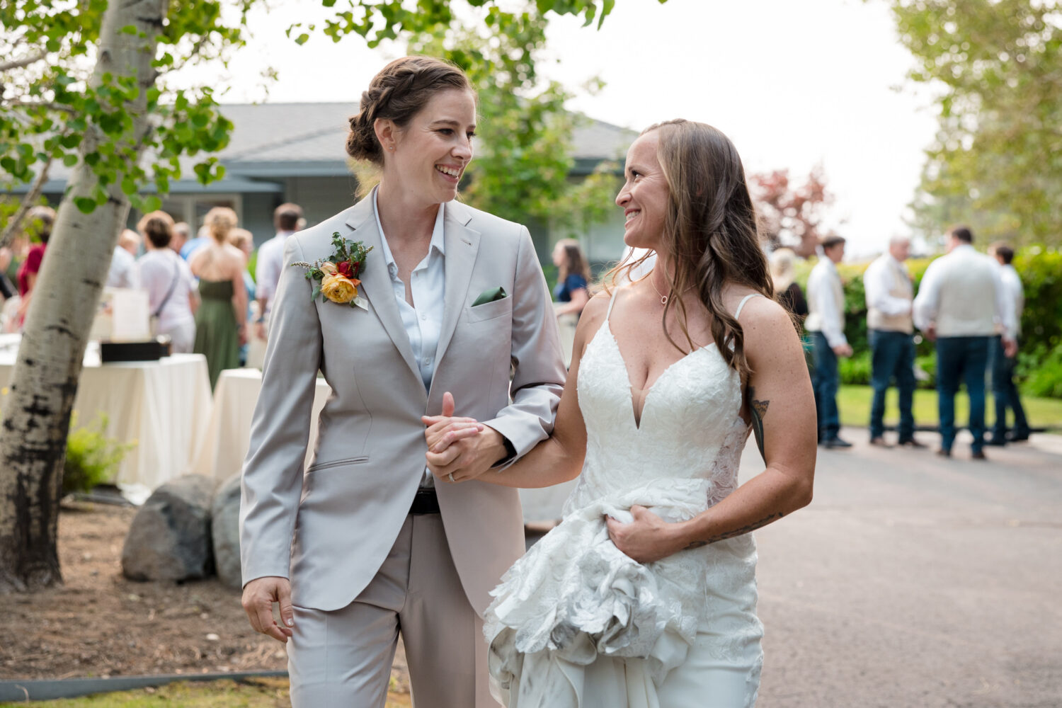 Two brides walk hand-in-hand at their backyard wedding.