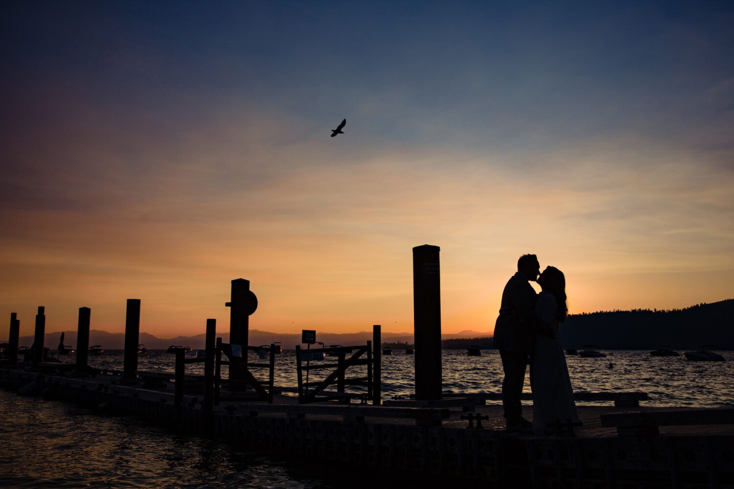 A romantic sunset kiss for a bride and groom in front of the floating Pier 111 Bar at Hyatt Tahoe.
