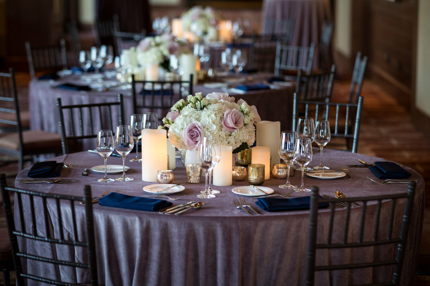 Round table setup for wedding reception with purple tablecloth and blue napkins. 